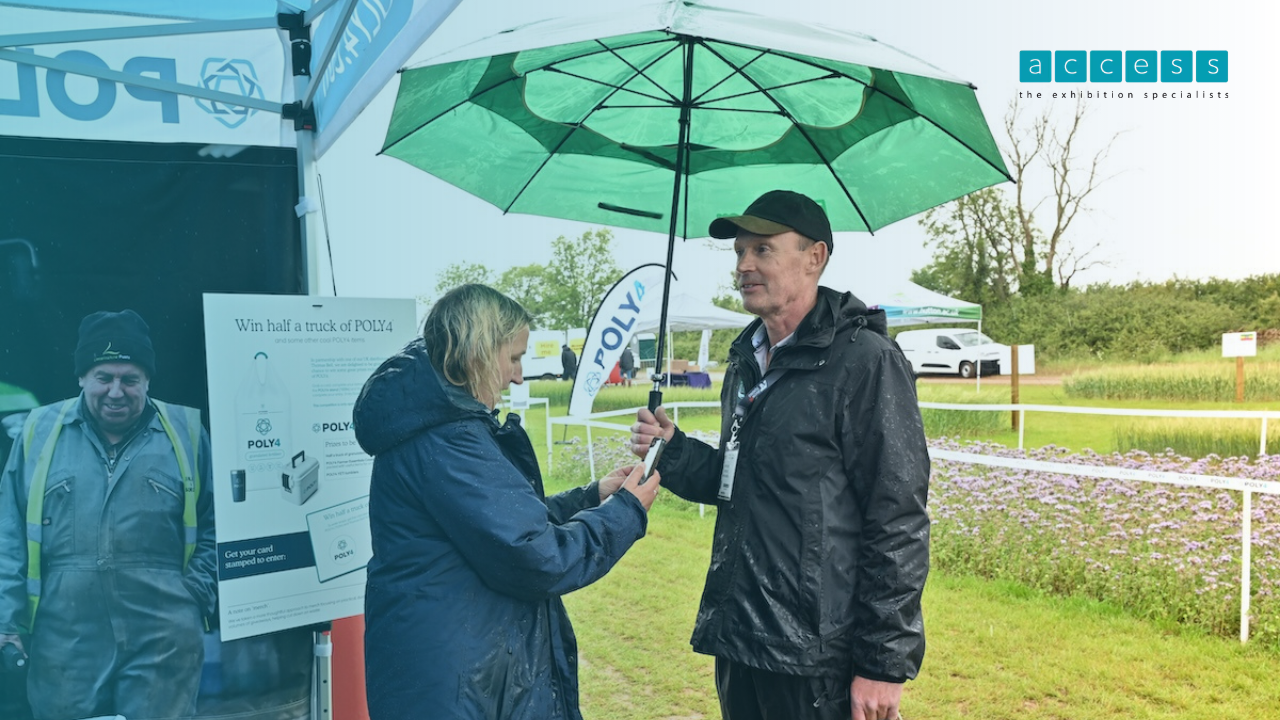 cereals-2026-outdoor-exhibition-stand-rain Access exhibition specialists team member greeting a visitor under an umbrella at the Cereals 2026 outdoor stand in the rain.
