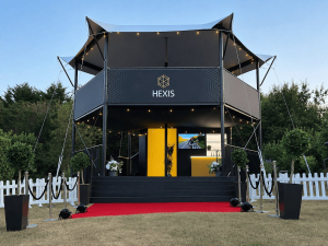 Hexis-Sky-Lounge-structure-dusk-picket-fence HEXIS elevated hospitality structure at dusk with white picket fence and red carpet, uplighting on stage.