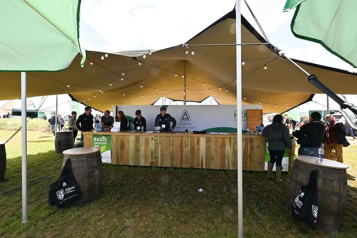 adama-stretch-tent-bar-wide-view-cereals-2026 Wide view of the ADAMA stretch tent bar with barrel tables and green parasols at Cereals 2026.