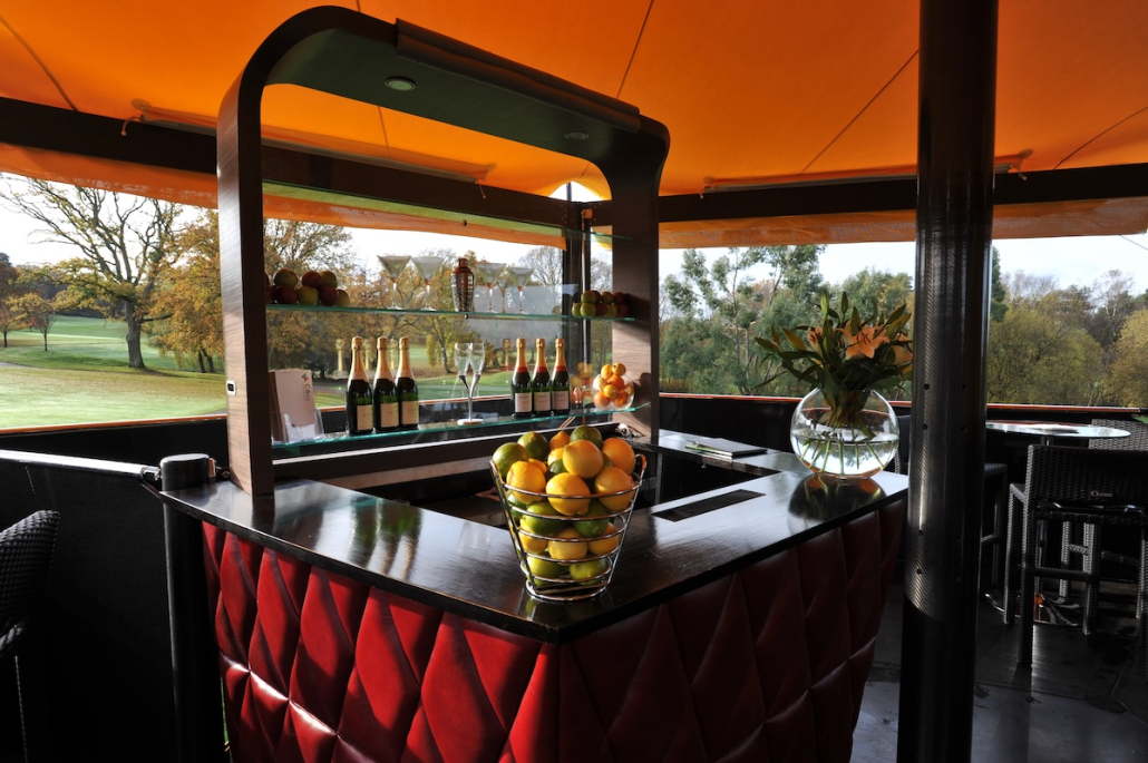 bespoke-hospitality-bar-interior-champagne-fruit-display Bespoke exhibition bar interior with red quilted panelling, champagne bottles and fresh fruit display overlooking parkland