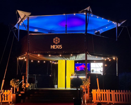 HEXIS elevated hospitality structure at night lit with blue canopy lighting and string lights.