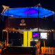 HEXIS elevated hospitality structure at night lit with blue canopy lighting and string lights.