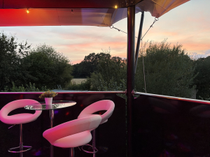 Pink lounge seating and table on an elevated hospitality structure balcony overlooking countryside at sunset