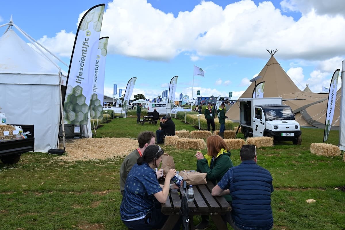 life-scientific-cereals-2026-outdoor-stand-visitors Visitors at picnic tables at the Life Scientific outdoor exhibition stand at Cereals 2026 with branded flags and tipis.