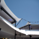 Underside view of stretch tent canopy roofing showing stage lighting rigs and string lights against a blue sky