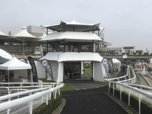 Three-storey white elevated exhibition structure at a racecourse with white canvas roofing.
