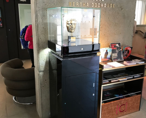 bafta-mask-glass-display-case-black-plinth BAFTA mask displayed in a glass case on a black lockable plinth at a cinema venue