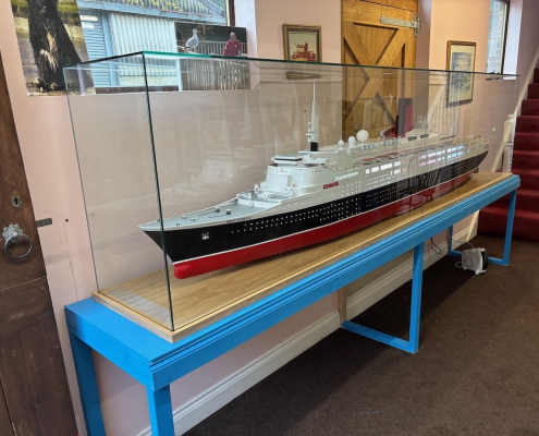 custom-glass-display-case-qe2-model-ship Custom glass display case housing a detailed QE2 model ship on a wooden and blue-framed console table