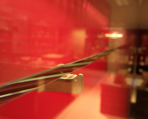 glass-shelf-bracket-detail-treasury-cabinet Close-up detail of a glass shelf bracket inside a red-lit treasury display cabinet