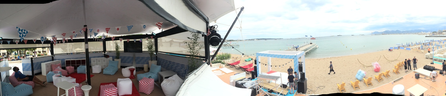HEXIS structures – beachfront lounge setup Panoramic view of a HEXIS beach lounge structure with striped seating and bunting, overlooking a seafront and pier