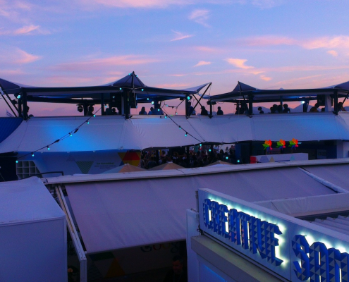 HEXIS rooftop hospitality venue at sunset with festoon lighting, marquee canopies and guests gathered on the terrace