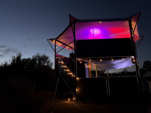 HEXIS structures – evening lighting in a garden setting HEXIS elevated structure illuminated with purple and pink canopy lighting and string lights at night in a rural garden setting
