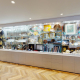 Long glass display cabinet with grey storage base showing an eclectic collection of glassware, ceramics, shells, books and a decorative robe
