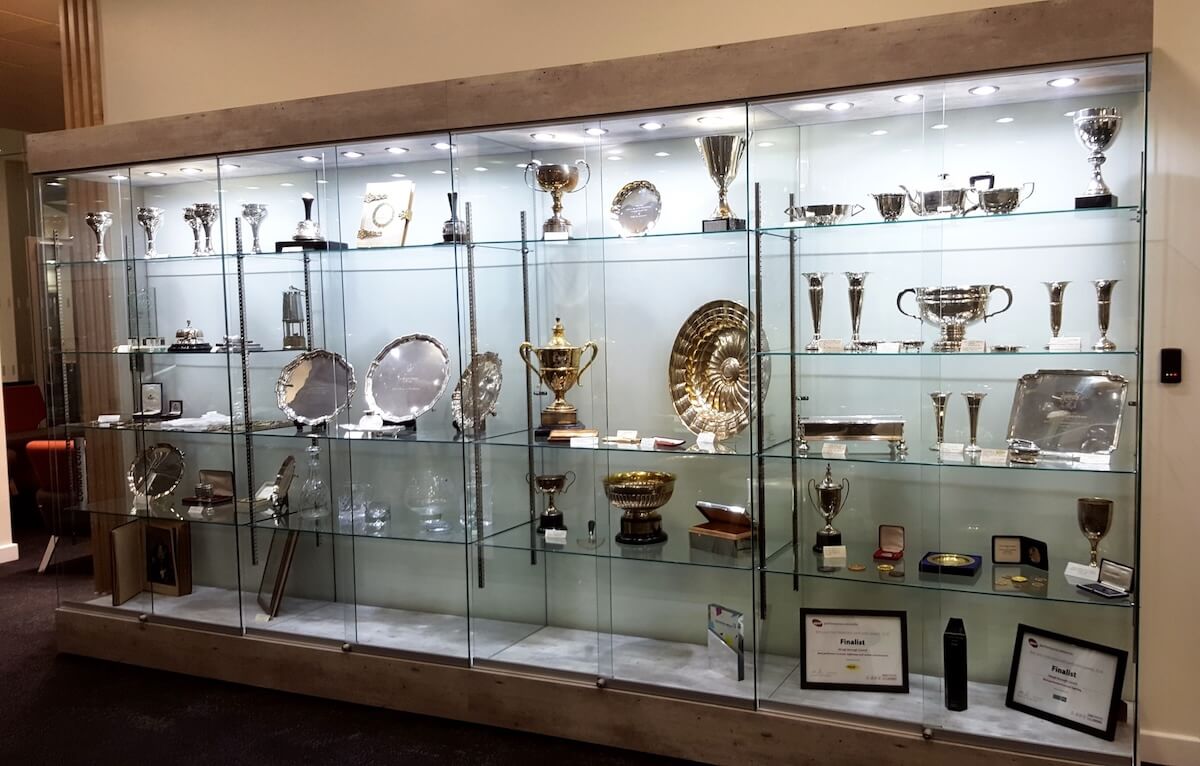 Wooden glass display cases – Slough Borough Council trophy cabinet Long wooden glass display cabinet at Slough Borough Council showcasing silver trophies, awards and finalist certificates