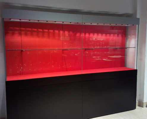 wall-mounted-glass-display-case-cathedral-treasury Wall-mounted glass display case with red illuminated backdrop and black storage base in a cathedral treasury