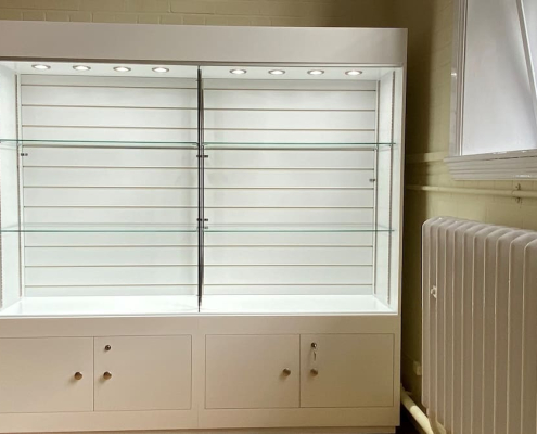 white-glass-display-cabinet-lit-shelving-lockable-storage White glass-fronted display cabinet with illuminated shelving and lockable storage cupboards below