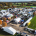 Aerial view of an outdoor trade show on a green showground in autumn, with white marquees, event structures and exhibitor stands set among orange and gold trees